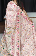 A woman modeling a light pink and beige printed saree with green and orange floral motifs and a pink border, paired with a dark blouse against a dark studio backdrop.